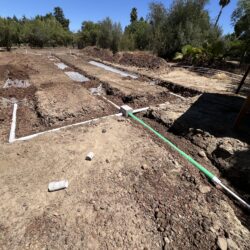 Underground plumbing installation with PVC pipes and conduit trenches for water or septic system in a construction site.